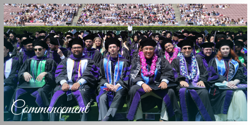 View of graduates seated in a row with the crowd in stadium seating behind them