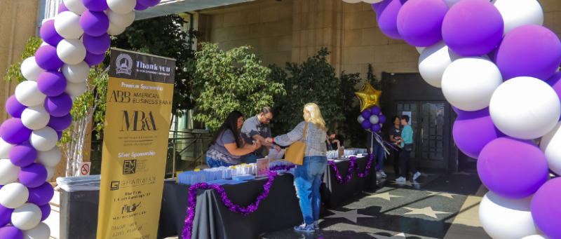 Guests checking in at table outside of Bullocks Wilshire building with purple and white balloon arch