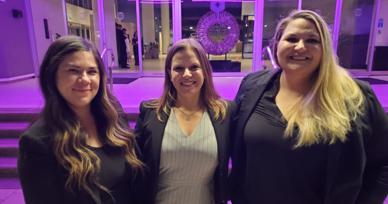Image - Moot Court Team ABA from left to right - Kelsi Grau, Alexandra Christensen, and Charlotte Bray in business formal wear standing outside under purple lighting