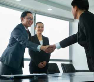 Three students in suits shaking hands across table