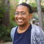 Professor Thompson-Bell headshot smiling at camera against greenery